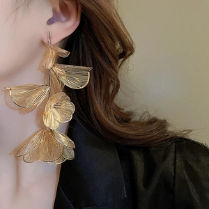 Detail of long gold tassel flower earrings with textured metallic finish on model