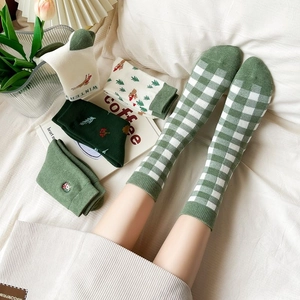 Close-up of green festive socks with elk embroidery and patterns on soft white bedding
