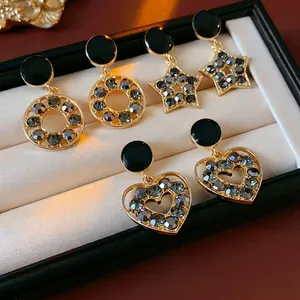 Boucles d'oreilles dorées avec étoile, cœur et strass noirs dans un écrin noir