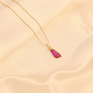 Collier doré avec pendentif en cristal violet posé sur du satin de soie beige