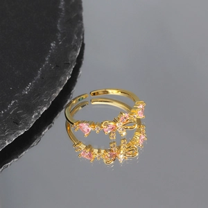 Detail of gold bow ring with pink heart cubic zirconia on grey mirror surface
