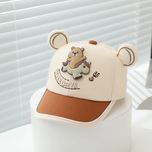 Gros plan sur la broderie d'ours et les oreilles 3D d'une casquette beige pour enfant