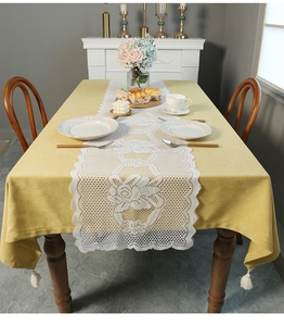 Close-up of ginger yellow tablecloth with white lace runner and pom pom fringe details