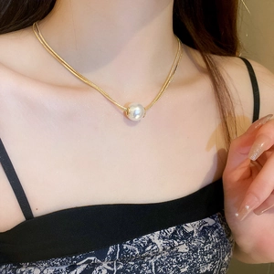 Detail of a gold double-layer chain necklace with a round white pearl on a model neck