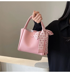 Detail of pink lychee leather bucket bag featuring decorative checkered silk scarf knot
