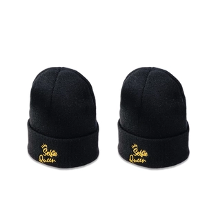 Pair of black knit beanies with yellow Selfie Queen crown embroidery on white background