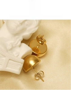 Close-up of minimalist gold dome earrings on satin fabric with plaster sculpture detail