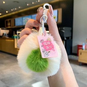 Detail of plush avocado keychain with pink Love tag held in hand in a cafe setting
