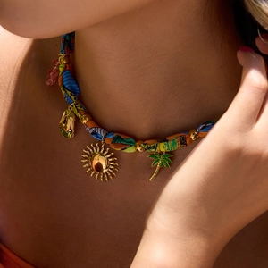 Close-up of summer charm necklace with ribbon, palm tree, sun and pink bear pendant