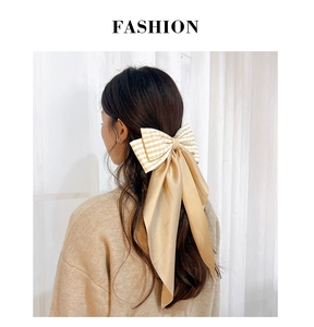 Detail of elegant cream plaid bow hair clip with long champagne satin ribbons on hair