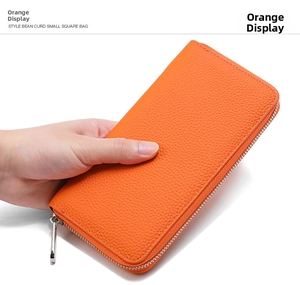 Detailed view of an orange pebble grain leather long wallet with silver zipper held in hand