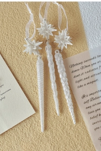 Detailed view of white glitter icicle Christmas ornaments with star-shaped tops and ribbons