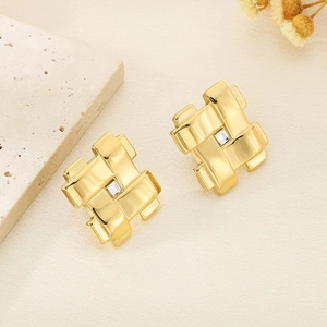 Détail de boucles d'oreilles dorées en résille avec diamant carré sur fond beige