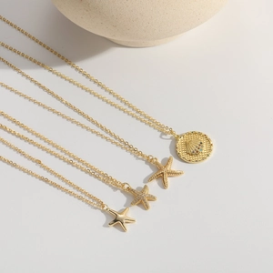 Gold starfish necklaces with shell motifs and zircon inlays on minimalist creamy background