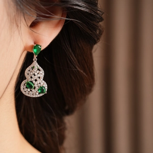 Close-up of silver hollow gourd earring with green gemstone and sparkling zircons