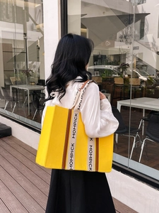 Large yellow felt tote bag with contrast MOMPICK straps shown in a street style street view