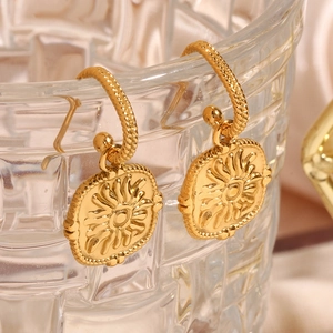 Close-up of vintage 18K gold plated sunburst earrings hanging on a textured glass cup