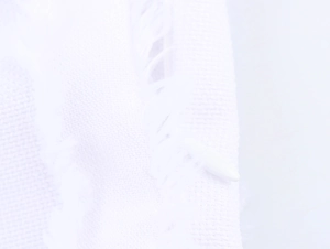 Close-up of white textured dress fabric showing detailed weave and fringe tassel edges