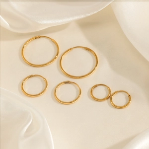 Three pairs of polished gold-plated stainless steel hoop earrings in tiered sizes on silk
