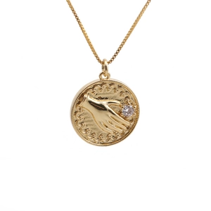 Collier doré tendance avec pendentif main et diamant sur fond blanc avec chaîne vénitienne