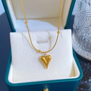 Detailed close-up of golden heart pendant necklace with bead chain in a jewelry box