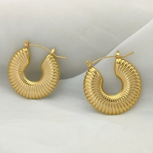 Macro shot of gold vintage U-shaped earrings with textured shell patterns on white cloth