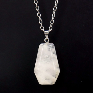 Macro detail of natural clear crystal coffin pendant with silver chain on black velvet