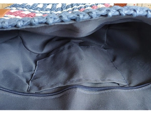 Detail view of the spacious navy blue lining and secure zipper pocket of a woven straw bag