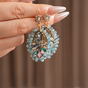 Gros plan de boucles d'oreilles ovales dorées avec perles bleues et cristaux colorés