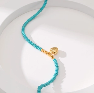 Handmade turquoise beaded necklace with a golden heart pendant on white pedestal