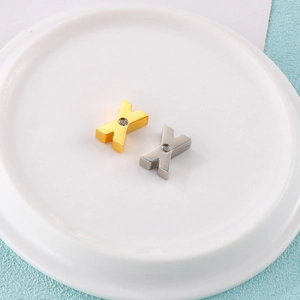 Golden and silver stainless steel letter X pendants with zircon inlay on a white plate