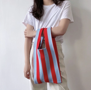 Chic red and blue striped knitted tote bag in vest shape held by a model on white background