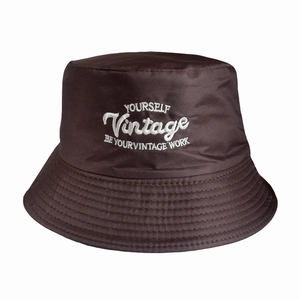 Detailed close-up of brown bucket hat featuring vintage white letter embroidery and stitching