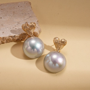 Elegant gold heart earrings with iridescent grey pearl on a textured stone background