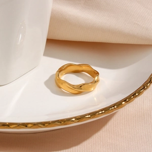 Macro shot of gold-plated geometric wavy ring on a ceramic plate with elegant shadows