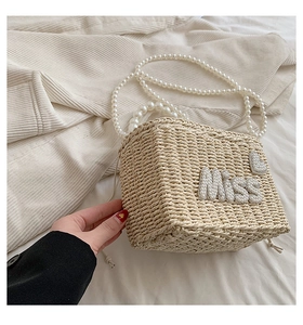 Detail of woven straw bag featuring pearl Miss lettering and a long pearl shoulder strap