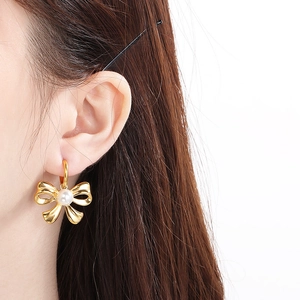 Detail view of a gold bow earring with a white pearl on a model for a chic style