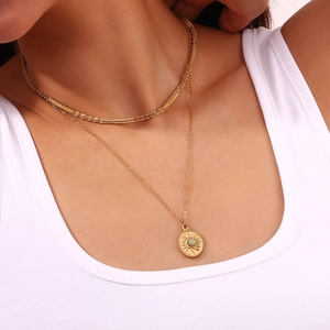 Detail of double-layer gold necklace with green stone sunburst pendant on female neck