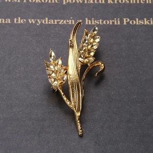 Close-up of golden wheat-shaped brooch with sparkling yellow crystals on a grey background