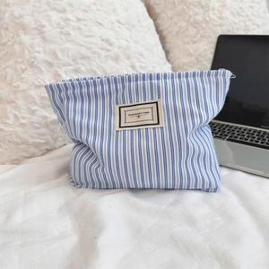 Detail of blue striped fabric toiletry bag with Pleasant Time label on soft bedding