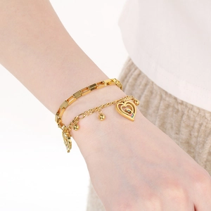 Detailed view of layered gold heart bracelet with beads on female wrist