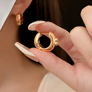 Close-up of sleek gold round hoop earrings featuring a minimalist metallic letter design