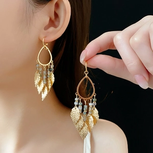 Détail de boucles d'oreilles feuilles dorées avec perles bleues sur modèle