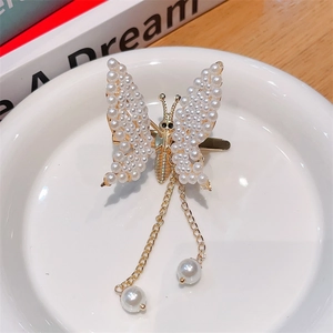 Detailed close-up of golden butterfly hair clip with white pearls and long tassels