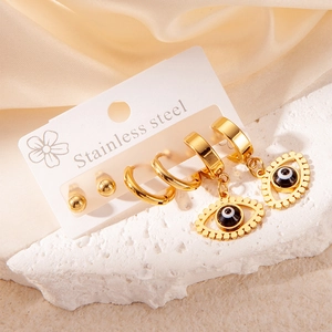 Detail of gold stainless steel eye pendant earrings set displayed on white brand card