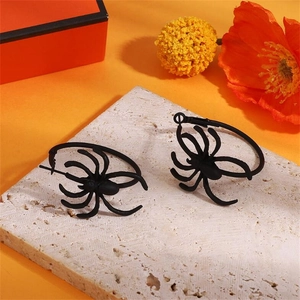 Gothic matte black spider hoop earrings on stone platform with orange background
