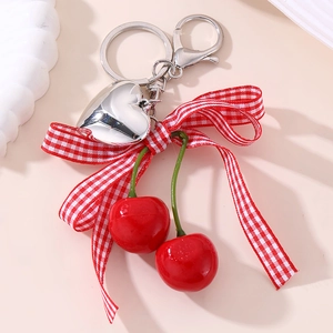 Close-up of heart keychain with red plaid ribbon bow and cherry pendants on pink background