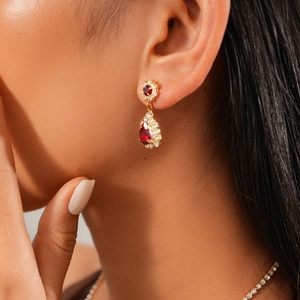 Close-up of luxury gold earrings with ruby-colored water-drop stones and diamond accents