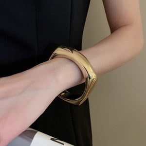 Gros plan sur un large bracelet manchette géométrique doré avec finition poli miroir