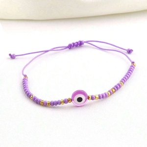 Close-up of purple woven evil eye bracelet with golden beads and adjustable sliding knot